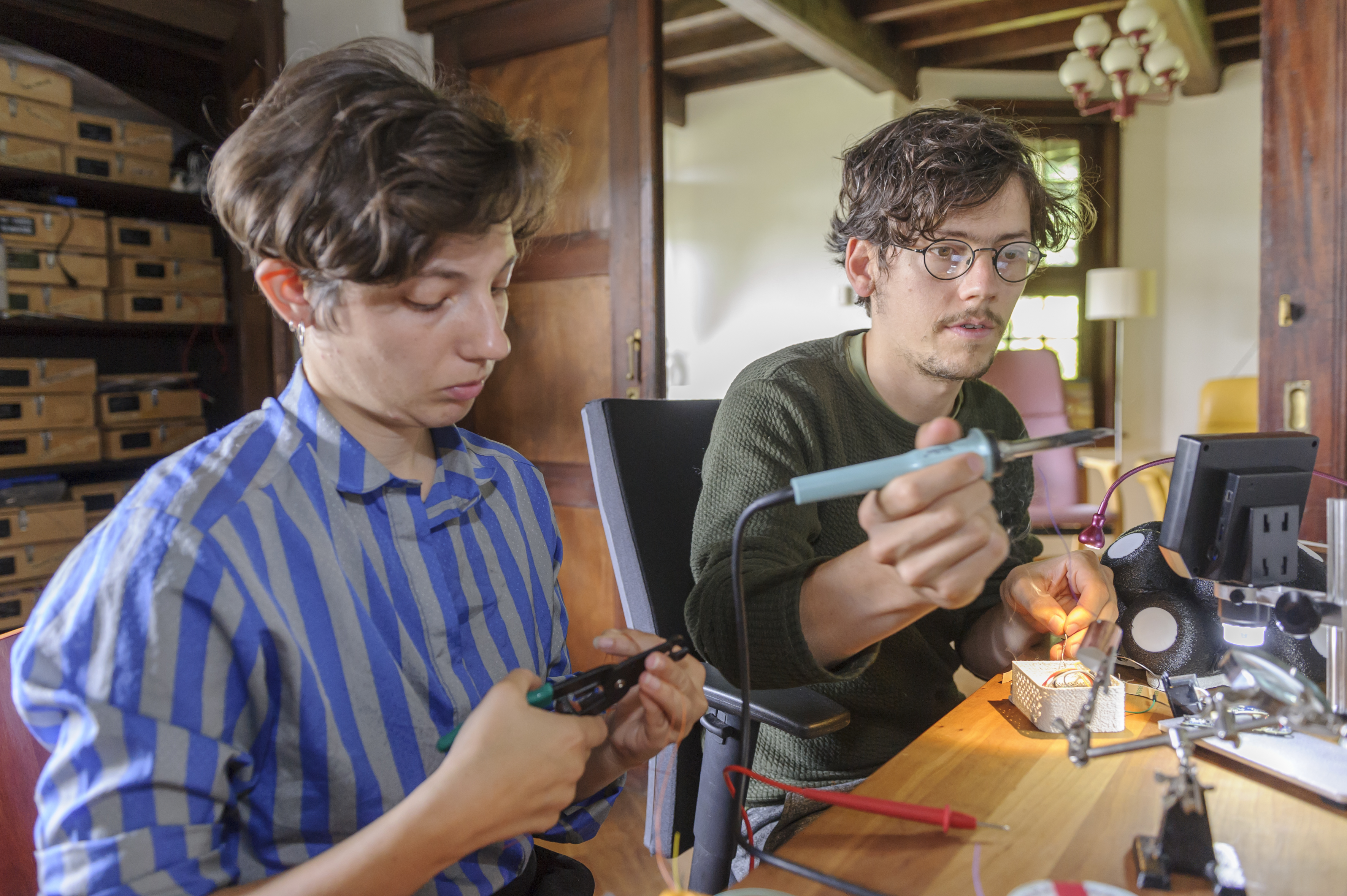 Arvid en Marie werken aan een tafel met soldeerbout en kniptang aan de Omniphone